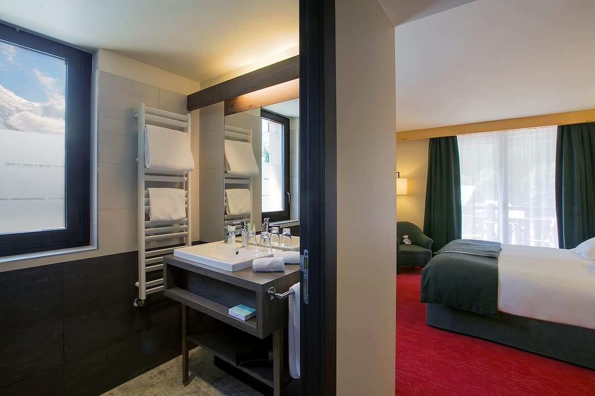 A hotel room with a large window, a bed, a bedside table, a mirror, and a built-in sink.
