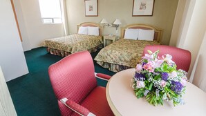 A hotel room with two beds, a red chair, a small table with a floral arrangement, and a window providing natural light. - San Francisco Business Class (Irapuato)