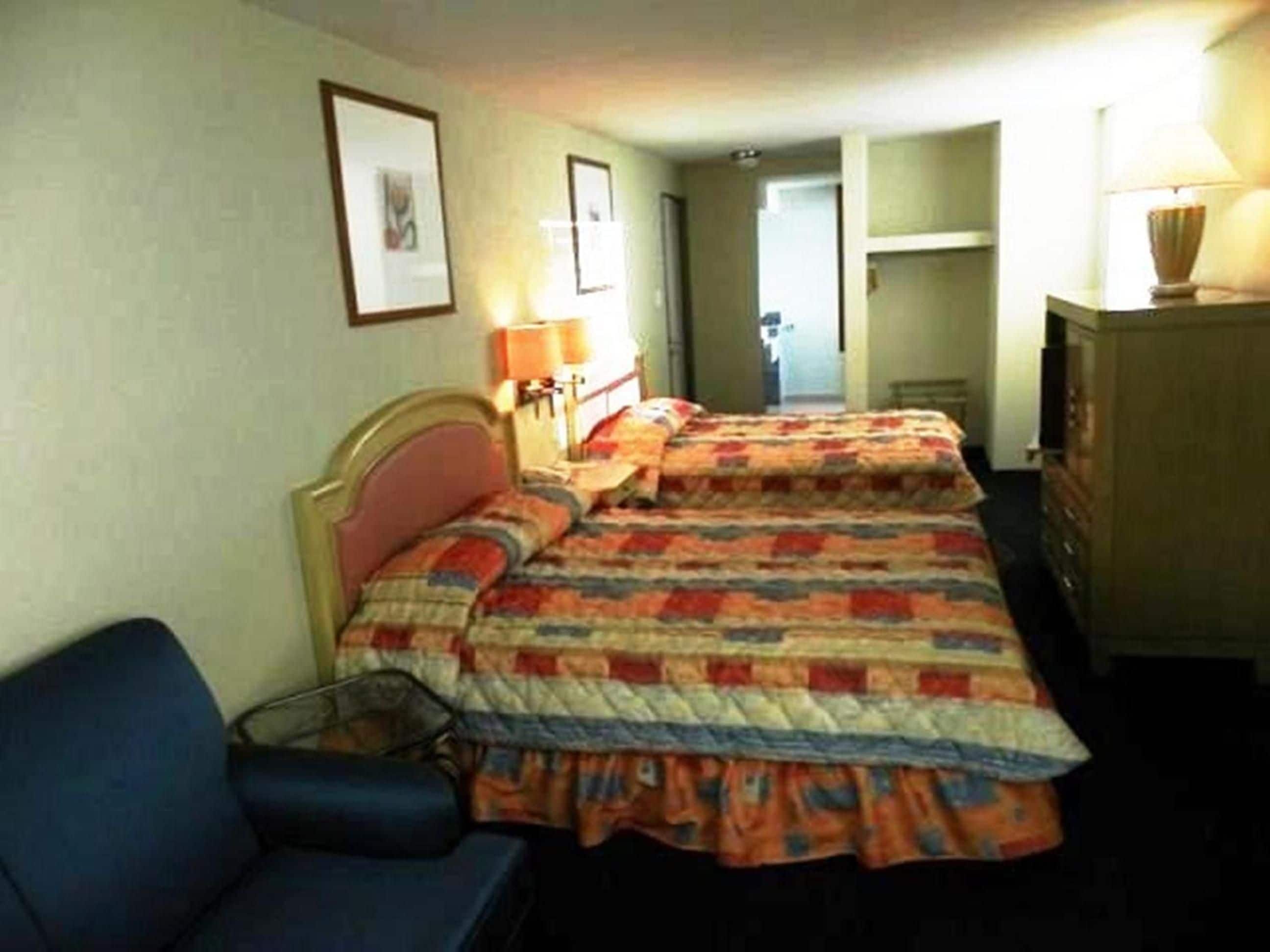 Quarto de hotel com cama, escrivaninha, cadeira e abajur.