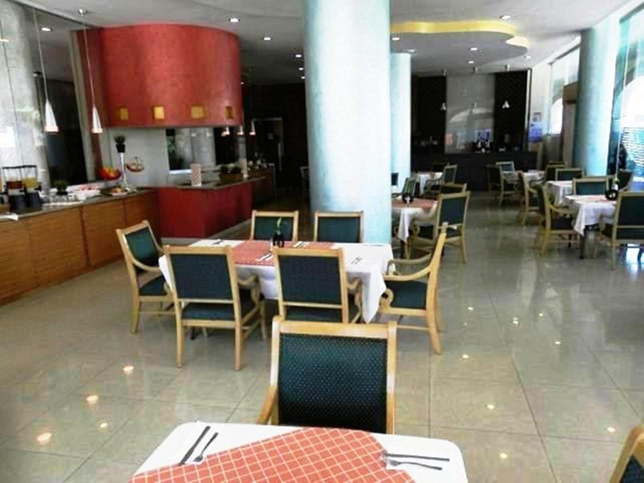 Un restaurante con mesas, sillas y una barra, además de un pilar rojo.
