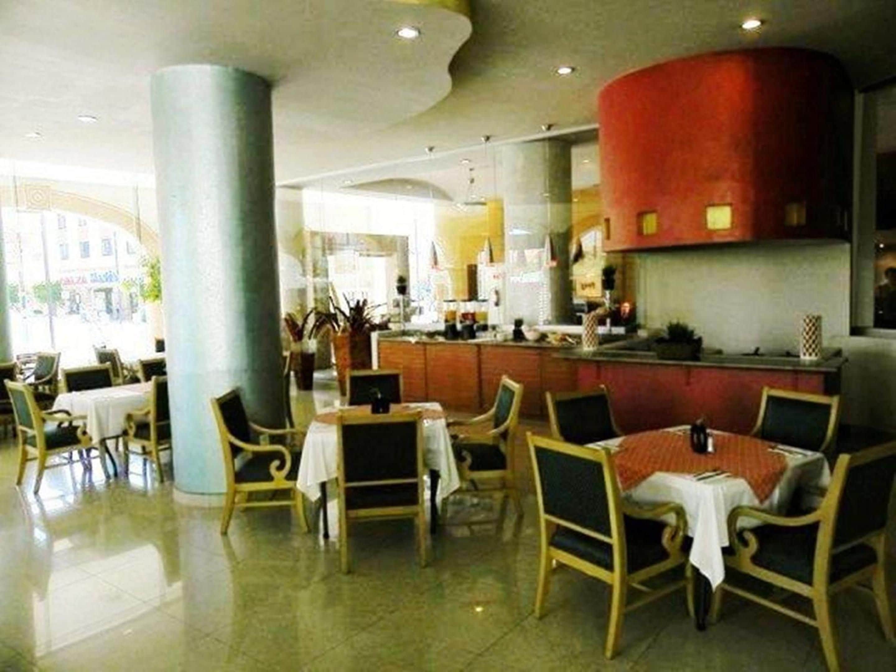 Una hall d'albergo con una zona bar centrale, diverse disposizioni di posti a sedere e vista sulla strada.