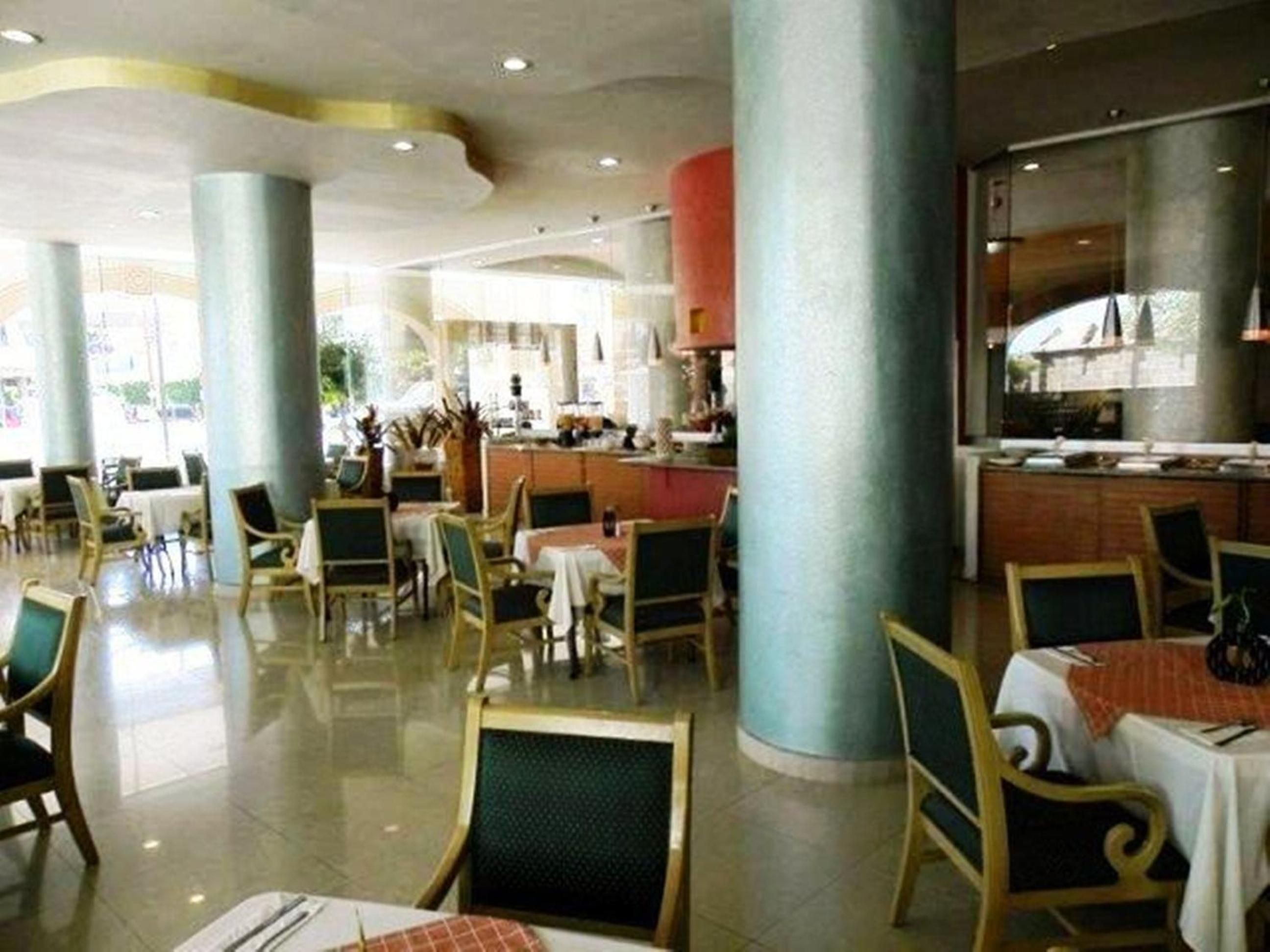 Un vestíbulo de hotel con una zona de bar central, arreglos de asientos y vista a la cocina al fondo.