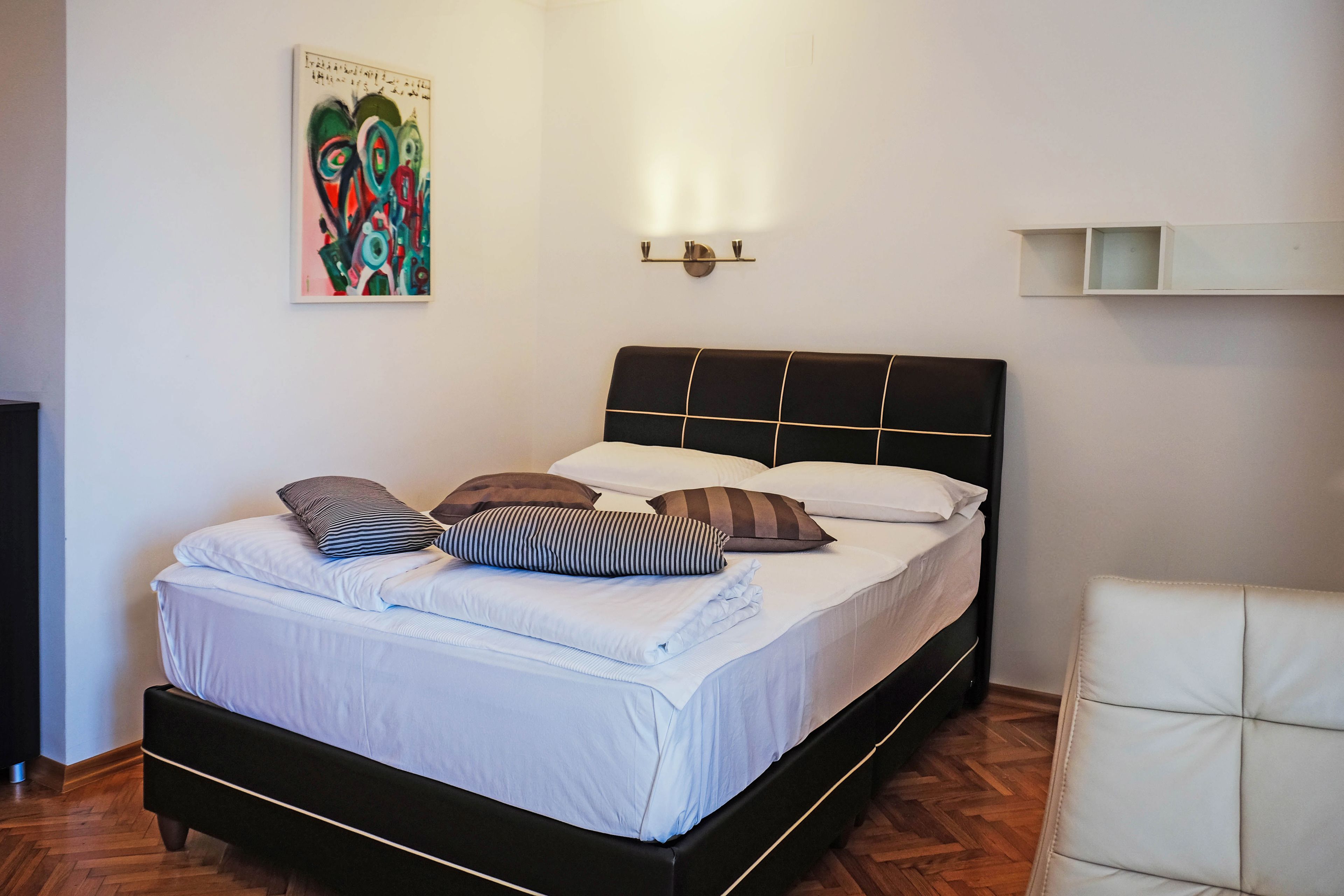 A neatly made bed with white linens and multiple pillows, a black headboard, and a wall-mounted light fixture.