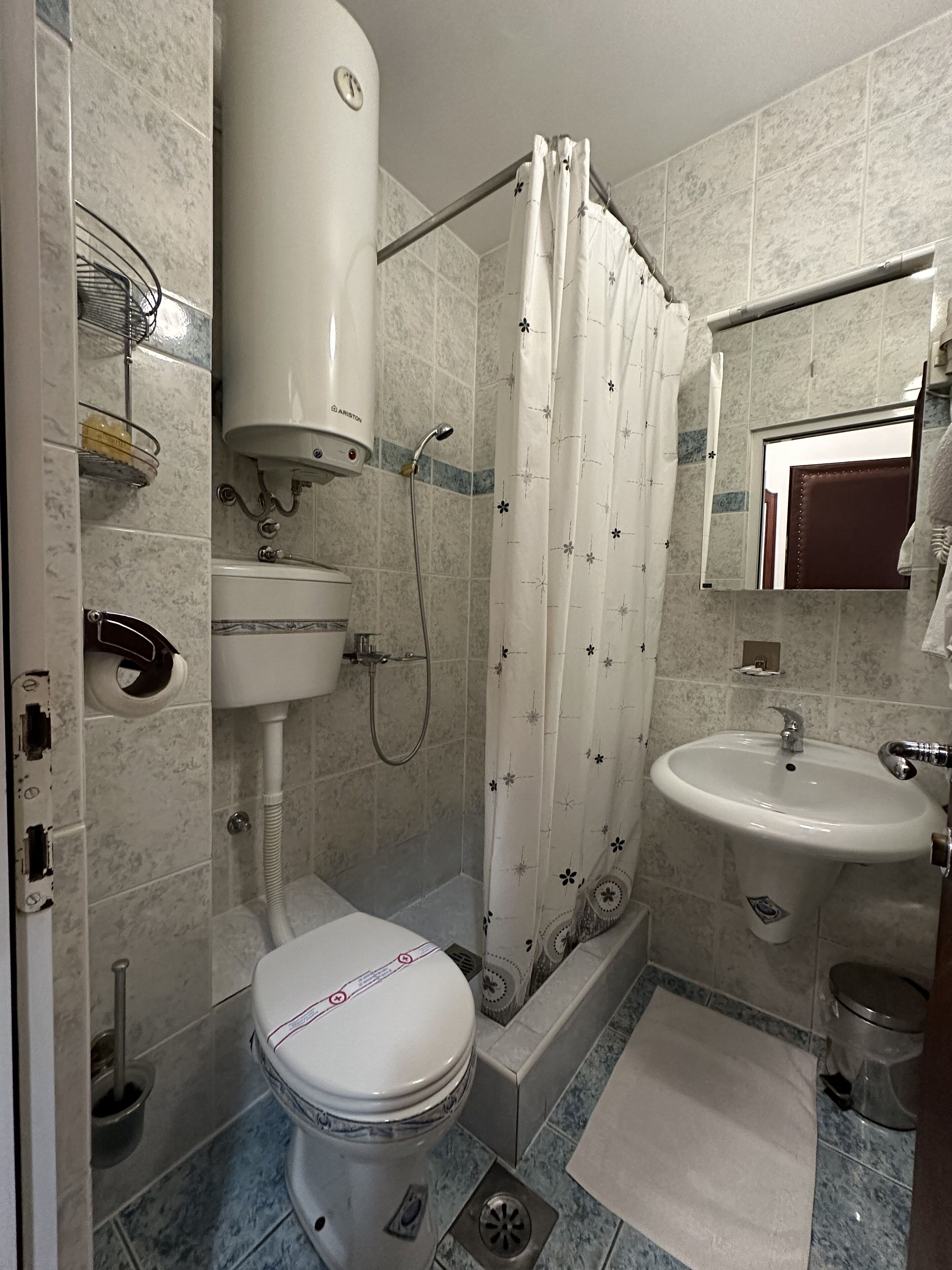 Un baño con inodoro, ducha, lavamanos y espejo.