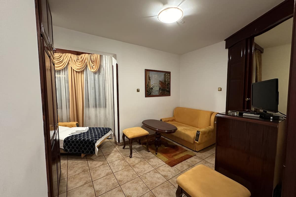 Una habitación de hotel con una cama, un sofá, una mesita, un televisor y un cuadro en la pared.