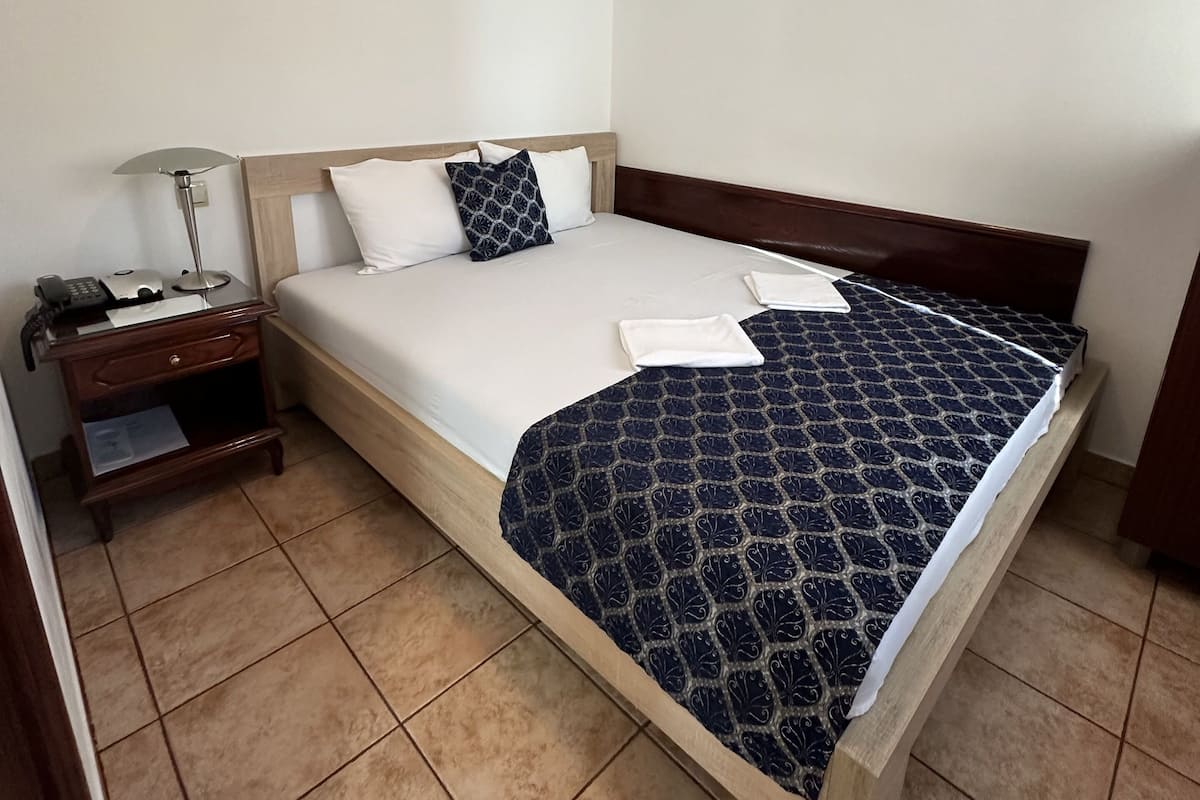 Una cama bien hecha con una colcha estampada, una mesita de noche con una lámpara y un cuadro en la pared.