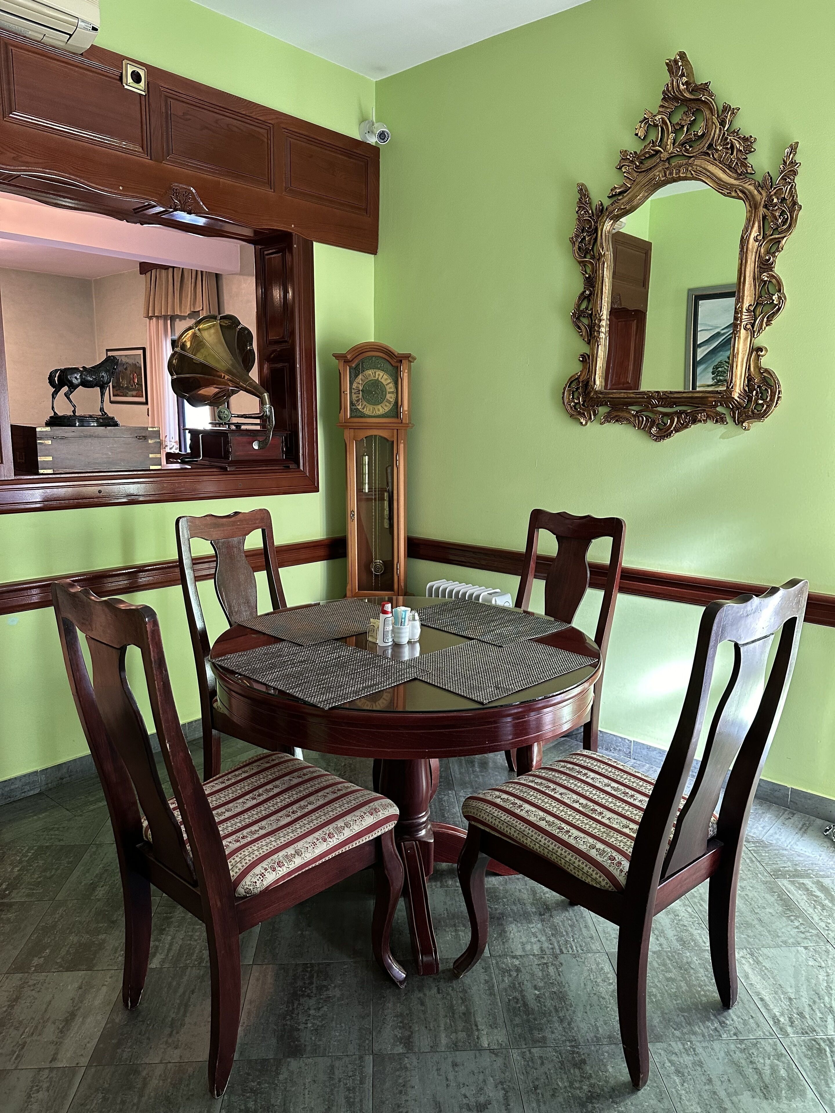 A dining area with a round table, four chairs, a clock, and a mirror on the wall.