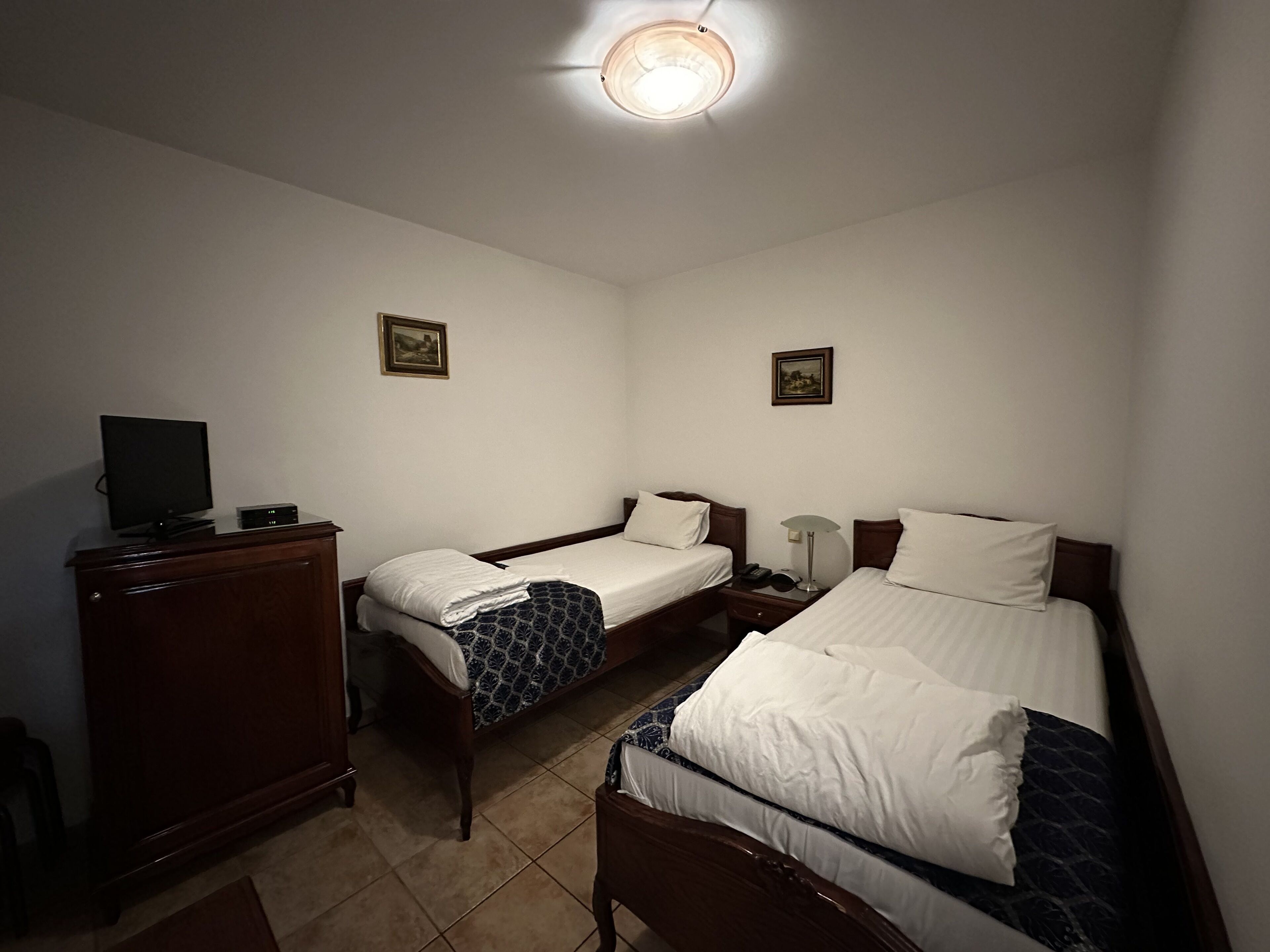 Una habitación de hotel con dos camas individuales, un aparador de madera, un televisor y dos cuadros colgados en la pared.