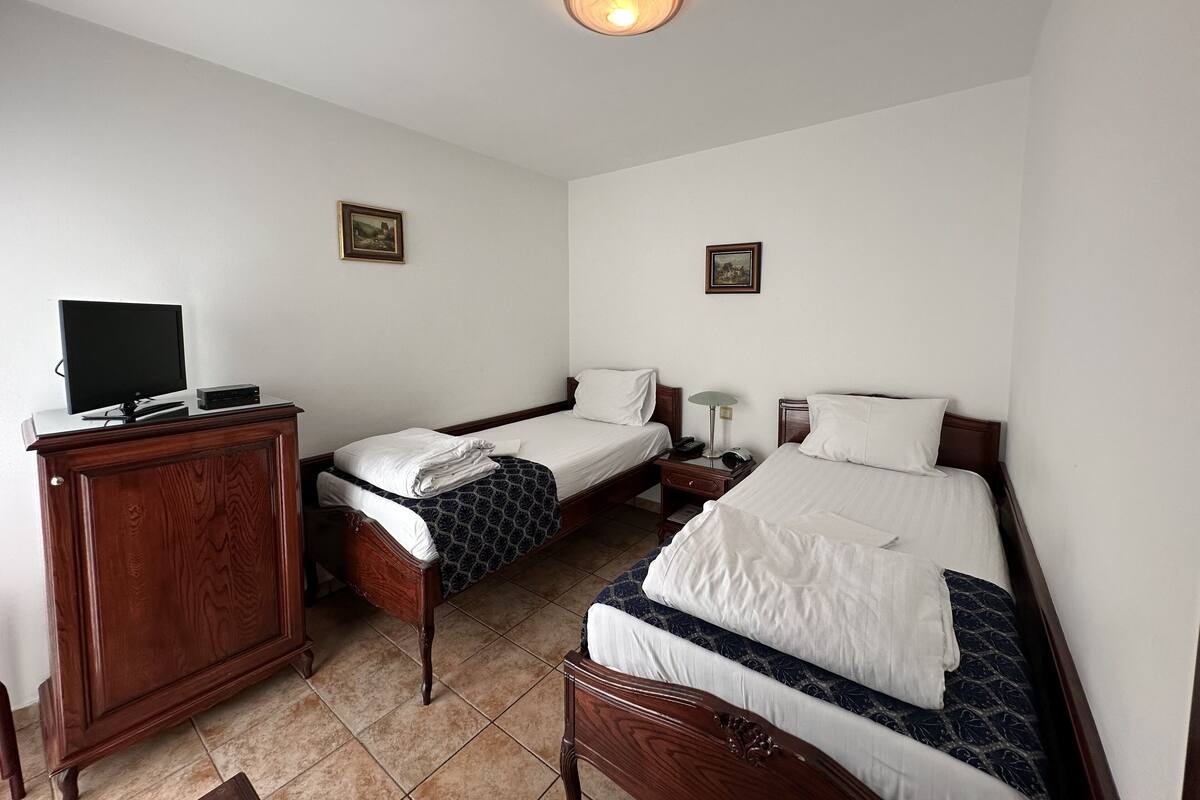 Una habitación de hotel con dos camas individuales, un armario de madera, un televisor y dos cuadros en las paredes.