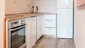 Una cocina moderna con armarios blancos, horno integrado, refrigerador y cafetera.