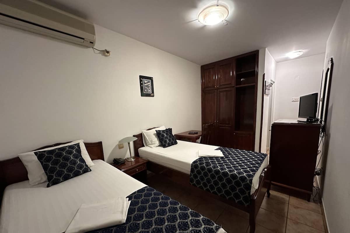 Habitación de hotel con dos camas, un escritorio, un armario y un televisor.