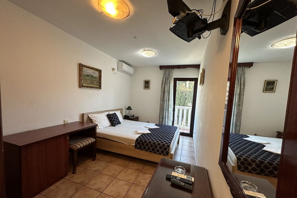 Habitación de hotel con dos camas, un escritorio, una silla, una mesita con un control remoto y un balcón con vistas.