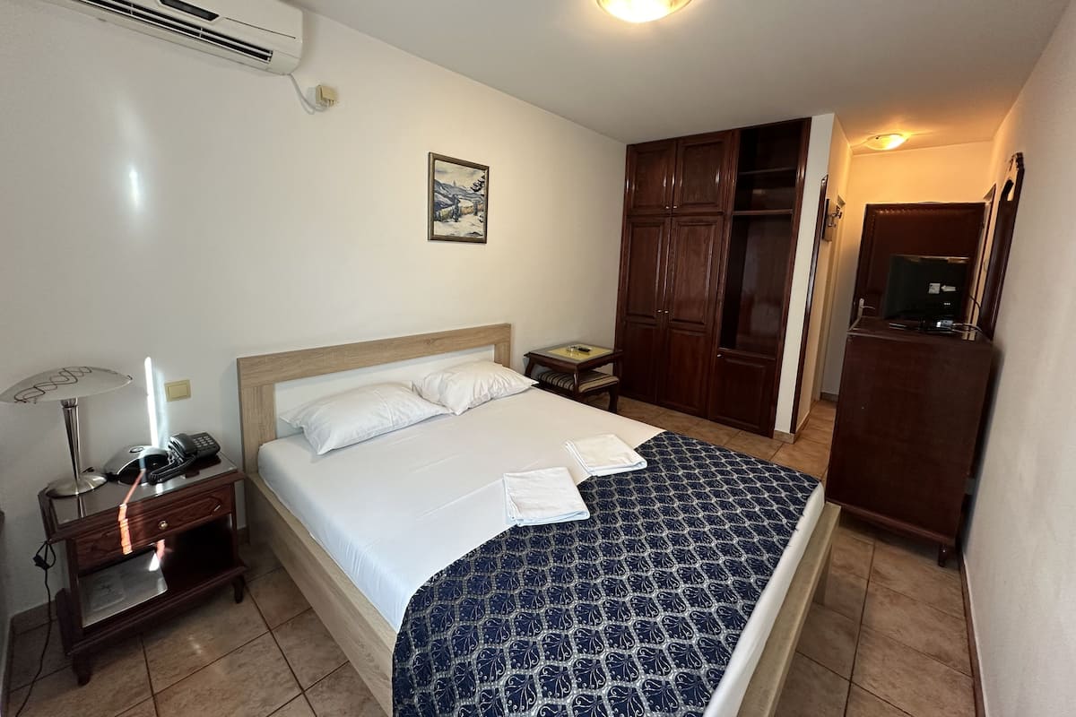 Una habitación de hotel con cama, armario, escritorio con lámpara y aire acondicionado.