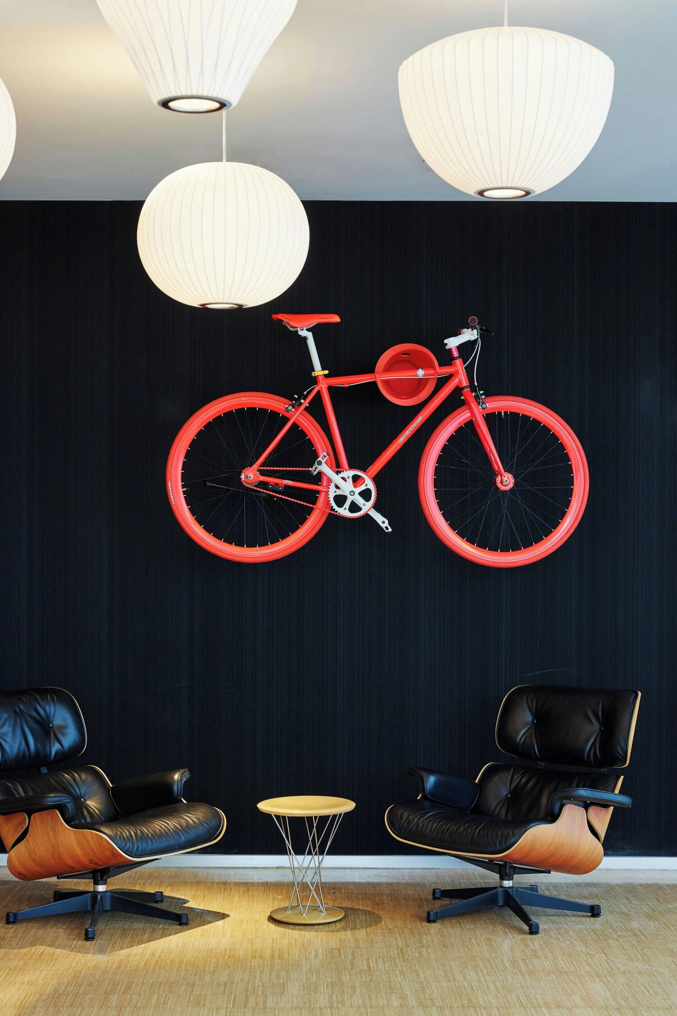 A room with a large wall-mounted bicycle, two leather chairs, a small round table, and three pendant lights.