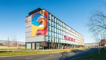 Un hotel moderno con un gran mural en la fachada, frontales de vidrio y un estacionamiento.
