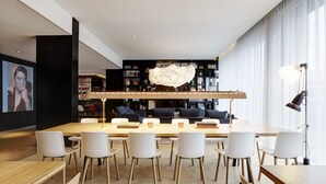 A modern library with a long wooden table, white chairs, and bookshelves filled with books and decorative items. - citizenM Amsterdam Airport Schiphol (Schiphol)