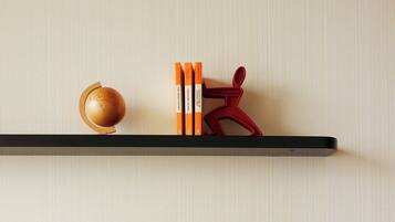 Habitación de hotel con una mesa redonda blanca, una silla roja, una estantería con libros y un objeto decorativo, además de una tableta mostrando un mensaje de bienvenida.