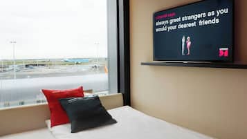 A hotel room with a television displaying a message, a bed with pillows, and a window overlooking an airport.