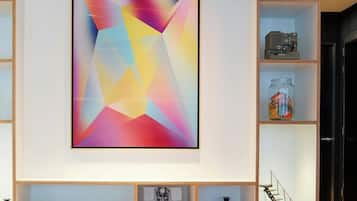 Una sala de estar moderna con un cuadro abstracto grande, estanterías de madera con libros y objetos decorativos, y una escalera que lleva a otro nivel.