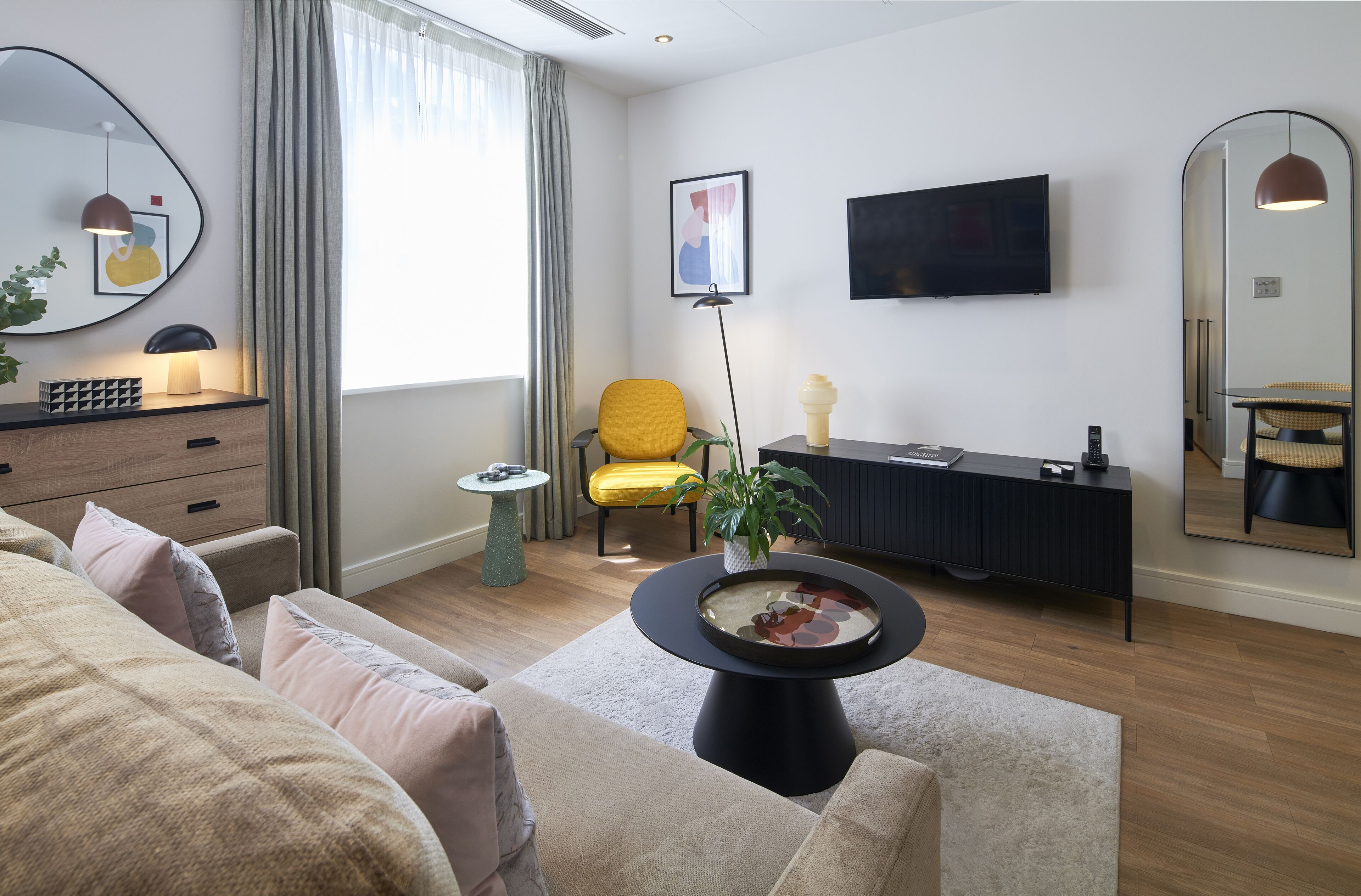 A modern living room with a sofa, a yellow chair, a round coffee table, a TV, and a large mirror.