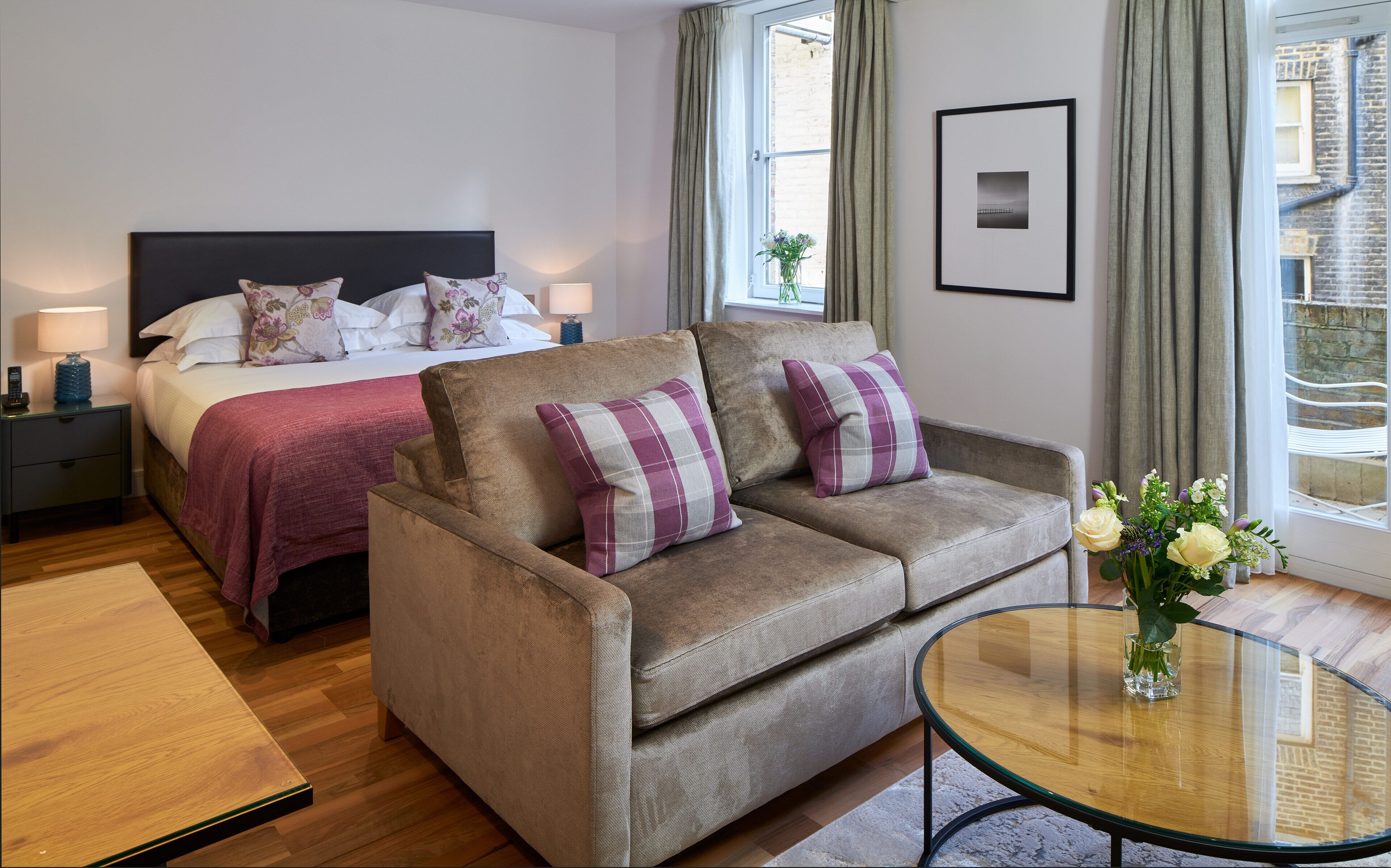 A hotel room with a bed, a sofa, a glass table, and a window with curtains.