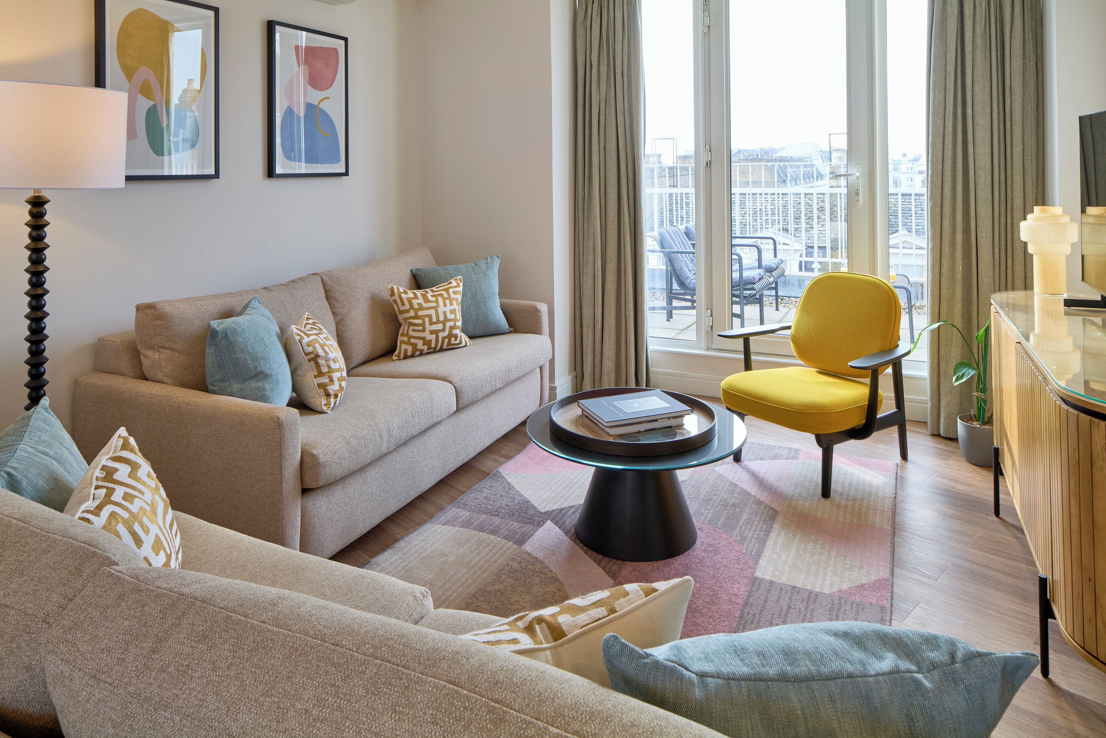 A modern living room with a sofa, armchair, and coffee table. There is a balcony with a view of the city.