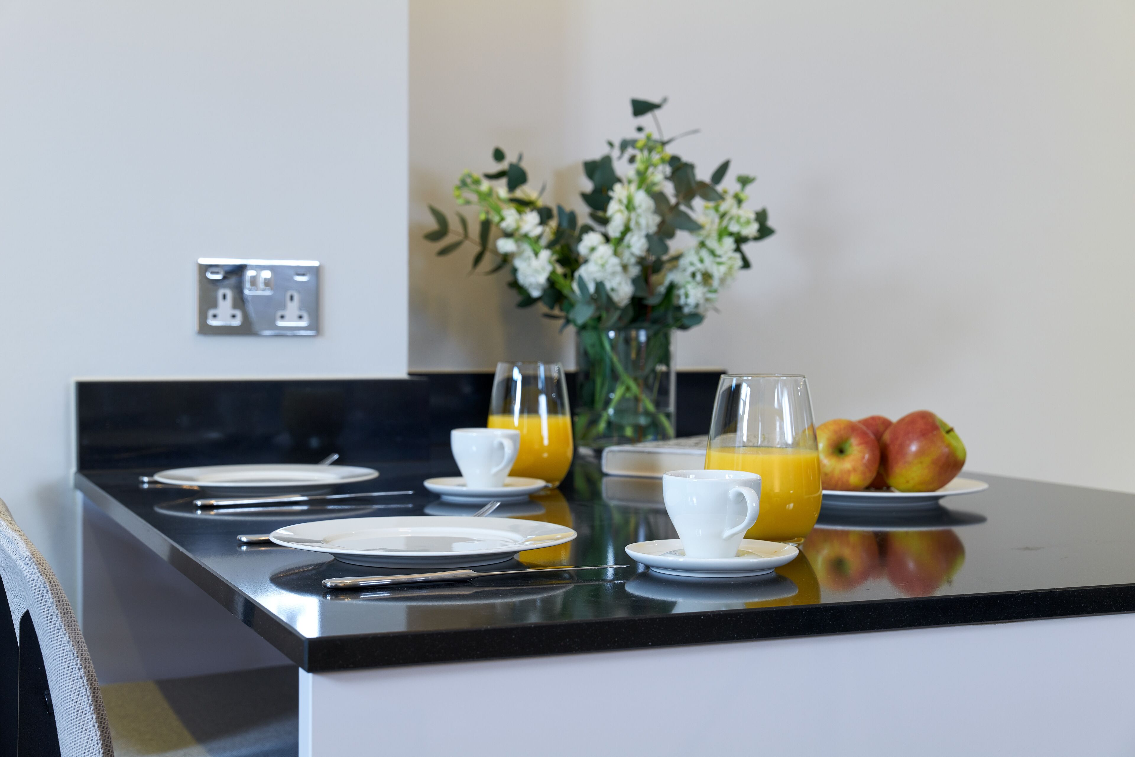 A breakfast setup with plates, cups, and a vase of flowers on a kitchen counter.