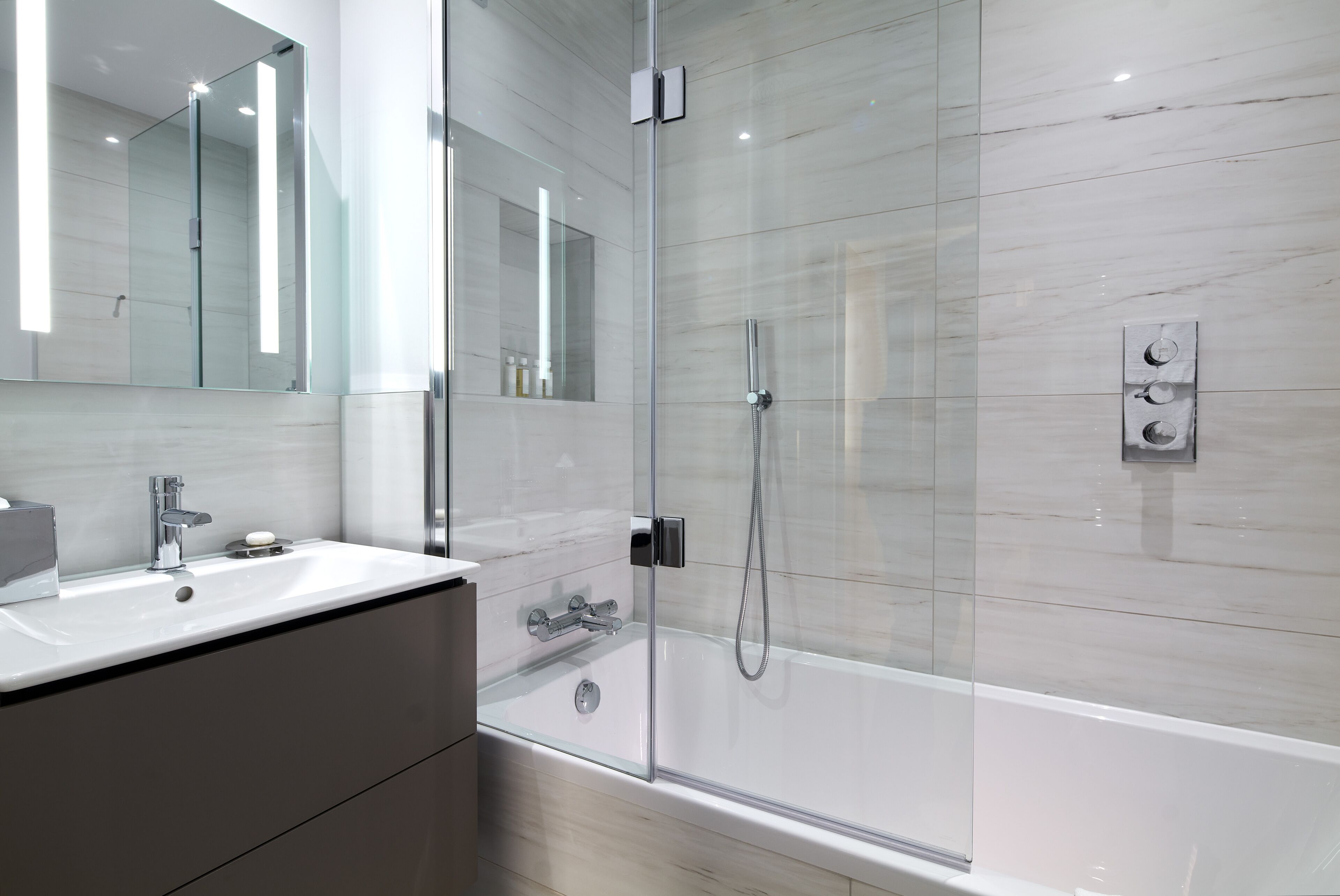 A modern bathroom with a glass-enclosed shower, a large mirror, and a white sink.