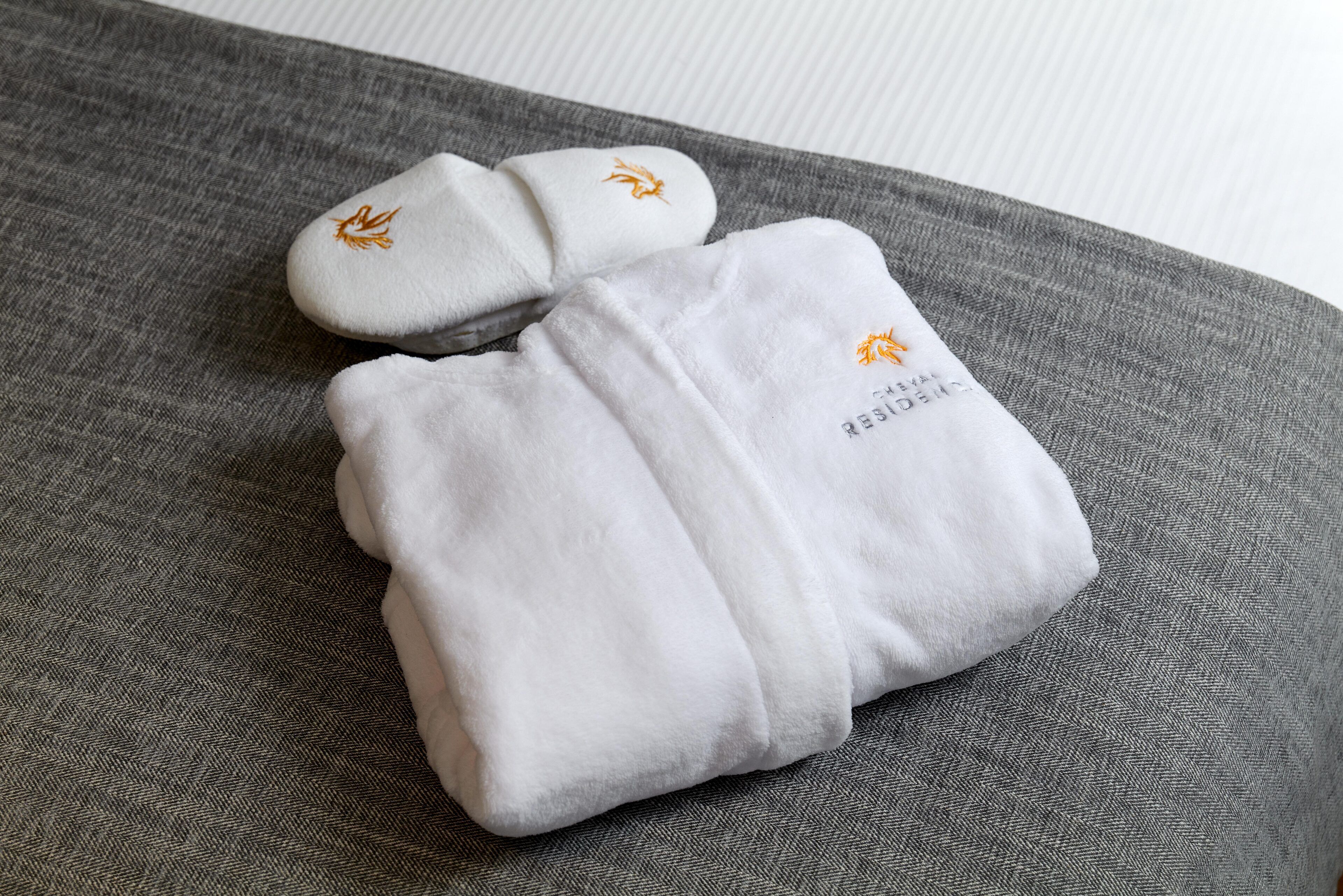 A neatly folded white towel with embroidered text and logo on a gray fabric surface.