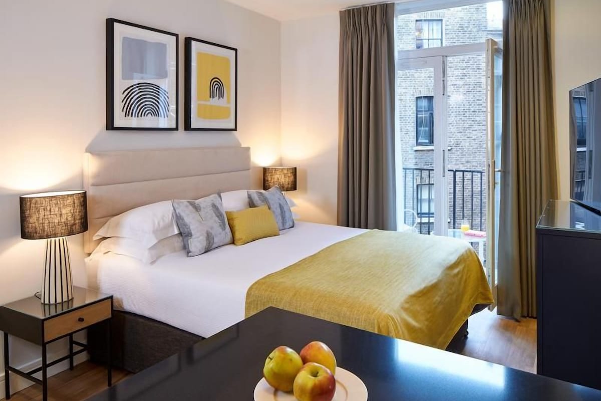 Une chambre d’hôtel avec un lit, des lampes de chevet, un bureau avec des pommes et des œuvres d’art accrochées au mur.