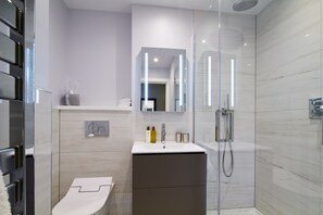 A modern bathroom with a glass-enclosed shower, a white sink, and a toilet. - Cheval Harrington Court at South Kensington (London)