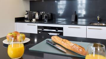 Una cocina moderna con cafetera, tostadora y lavamanos incorporados. Hay manzanas y una baguette en la encimera, y un vaso de zumo de naranja.