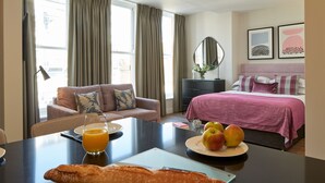 Camera d'albergo con un letto, una poltrona, un tavolo da pranzo con colazione e vista sulla città.