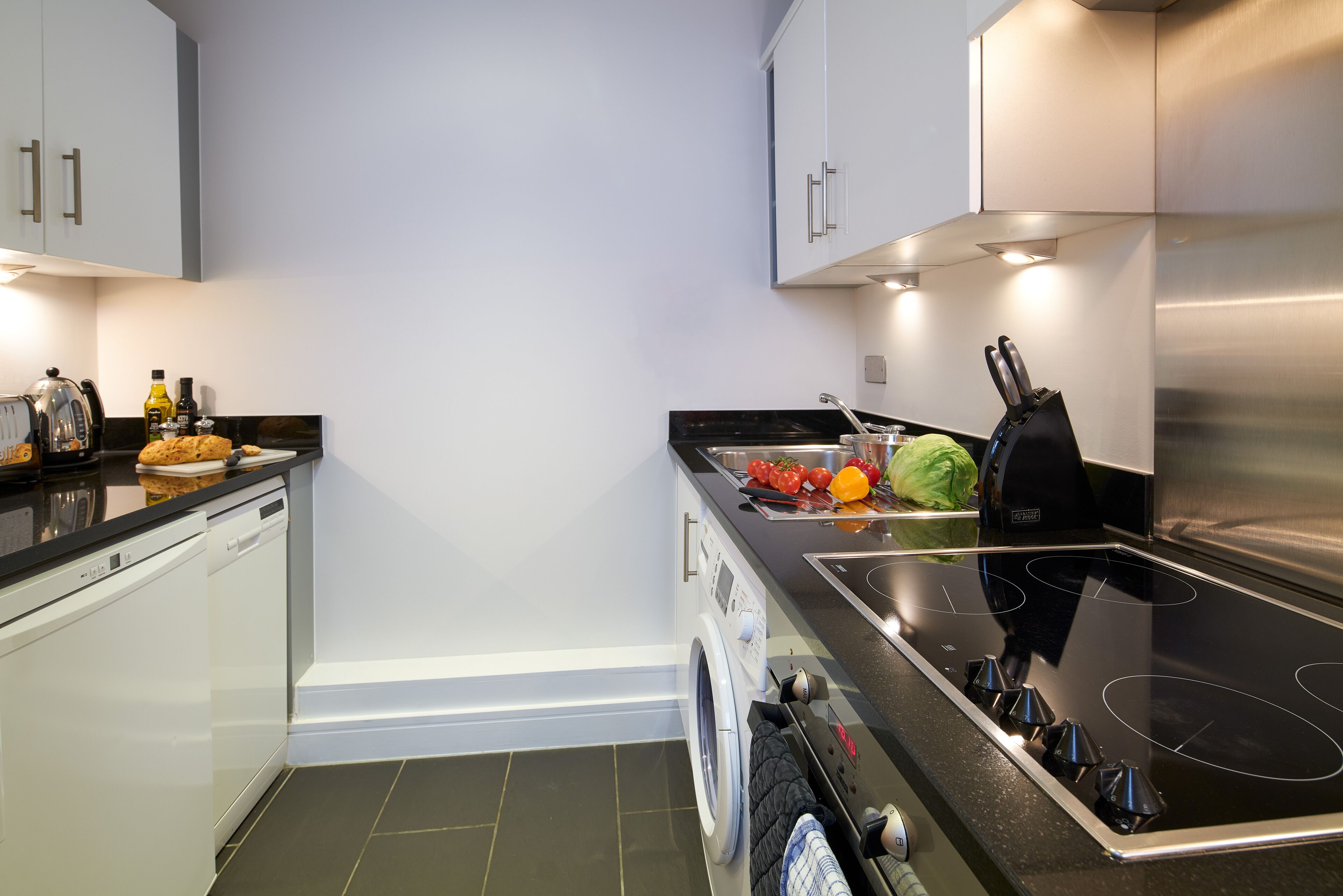 Une cuisine moderne équipée d’un lave-vaisselle, d’un lave-linge et d’une plaque de cuisson à induction noire.