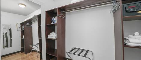 Et hotelværelse med trægulv, et stort spejl, et walk-in closet med hængende tøj og et håndklædestativ.