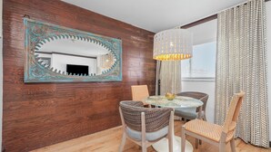 A dining area with a round table, four chairs, a decorative mirror, and a hanging lamp. - Metropole Suites South Beach (Miami Beach)