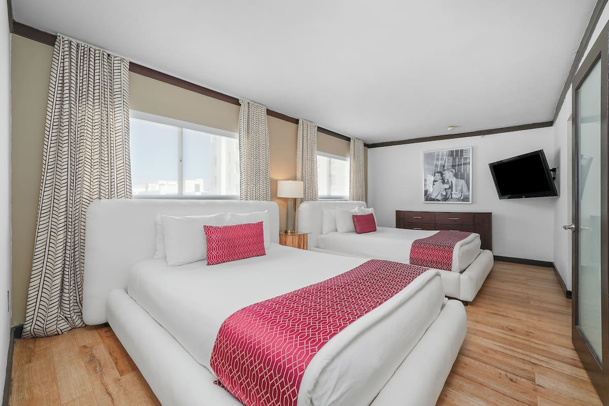 A hotel room with two beds, a TV, and a large window.