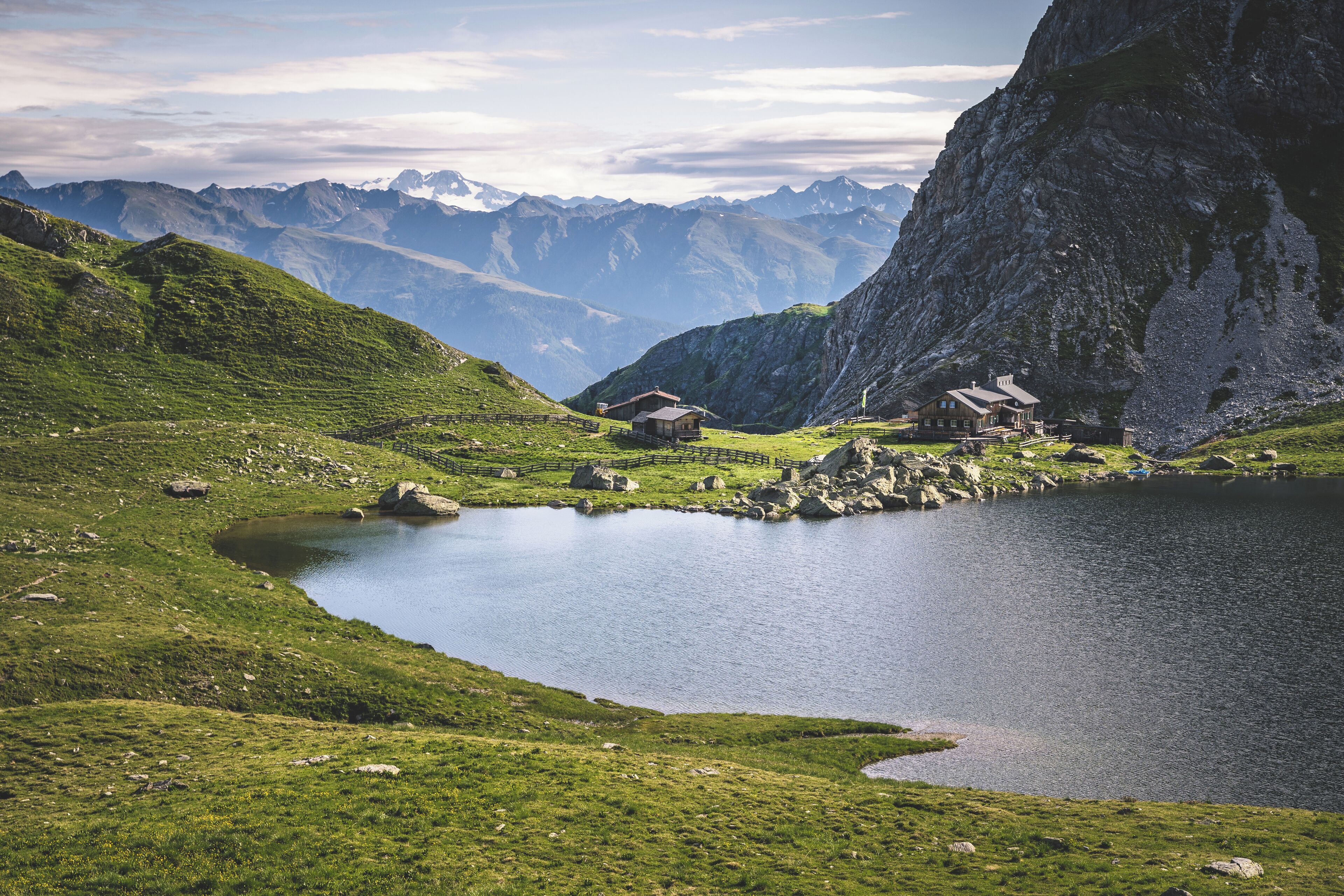 Un paysage montagneux avec un lac, un chalet en bois et une grande formation rocheuse.