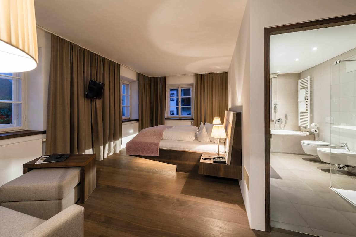 A hotel room with a bed, bedside lamps, a TV, a desk with a lamp, and a bathroom with a sink and toilet.
