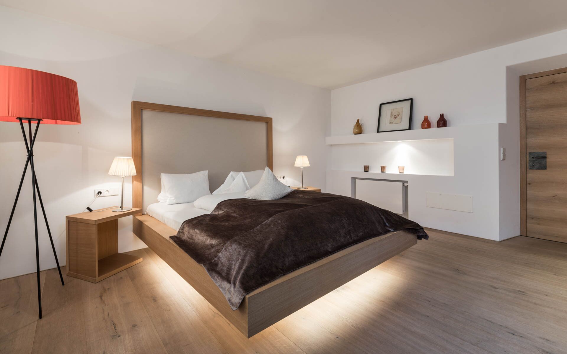 Un dormitorio moderno con estructura de cama de madera, ropa de cama blanca y una lámpara de pie roja.