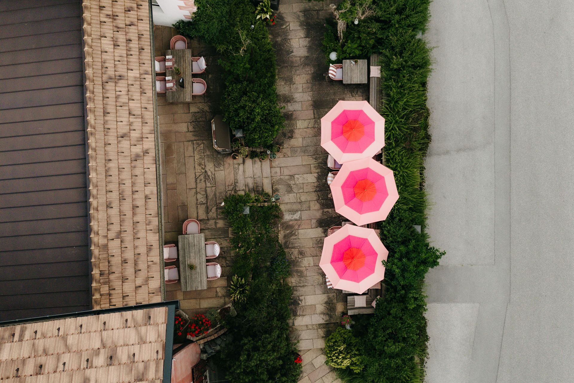 An outdoor patio area with stone flooring, wooden furniture, and multiple pink umbrellas.