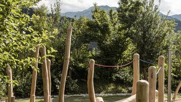 Estructura de juego de madera al aire libre en un parque con zona de césped y árboles de fondo.