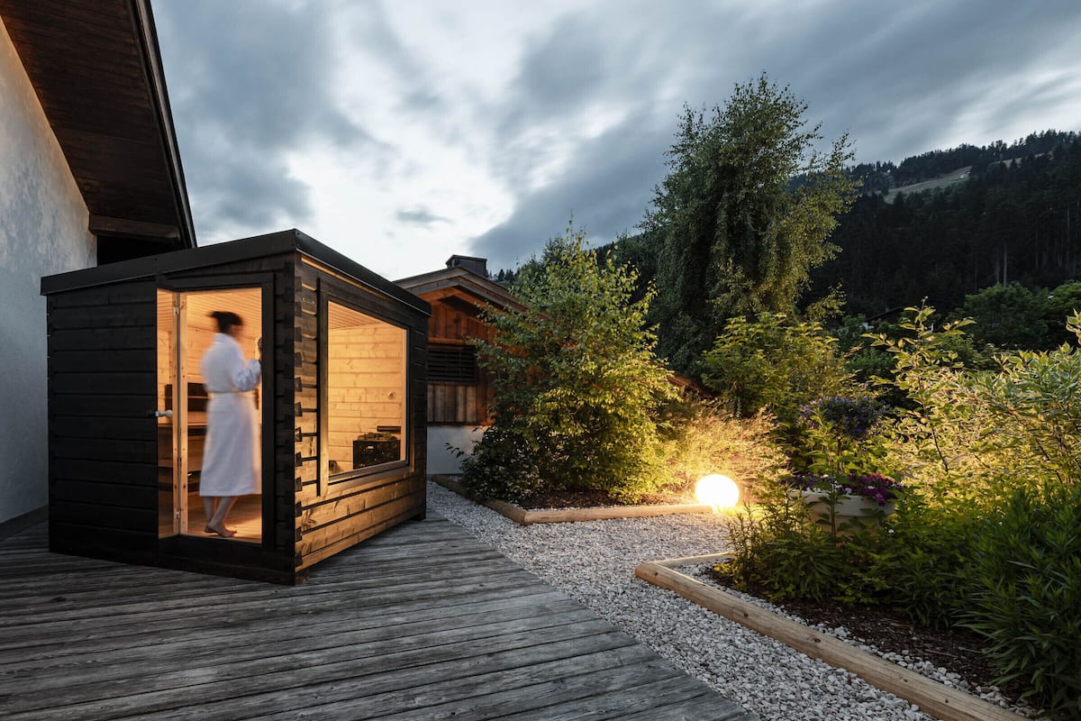 A wooden cabin with a person inside, surrounded by a garden and a wooden deck.