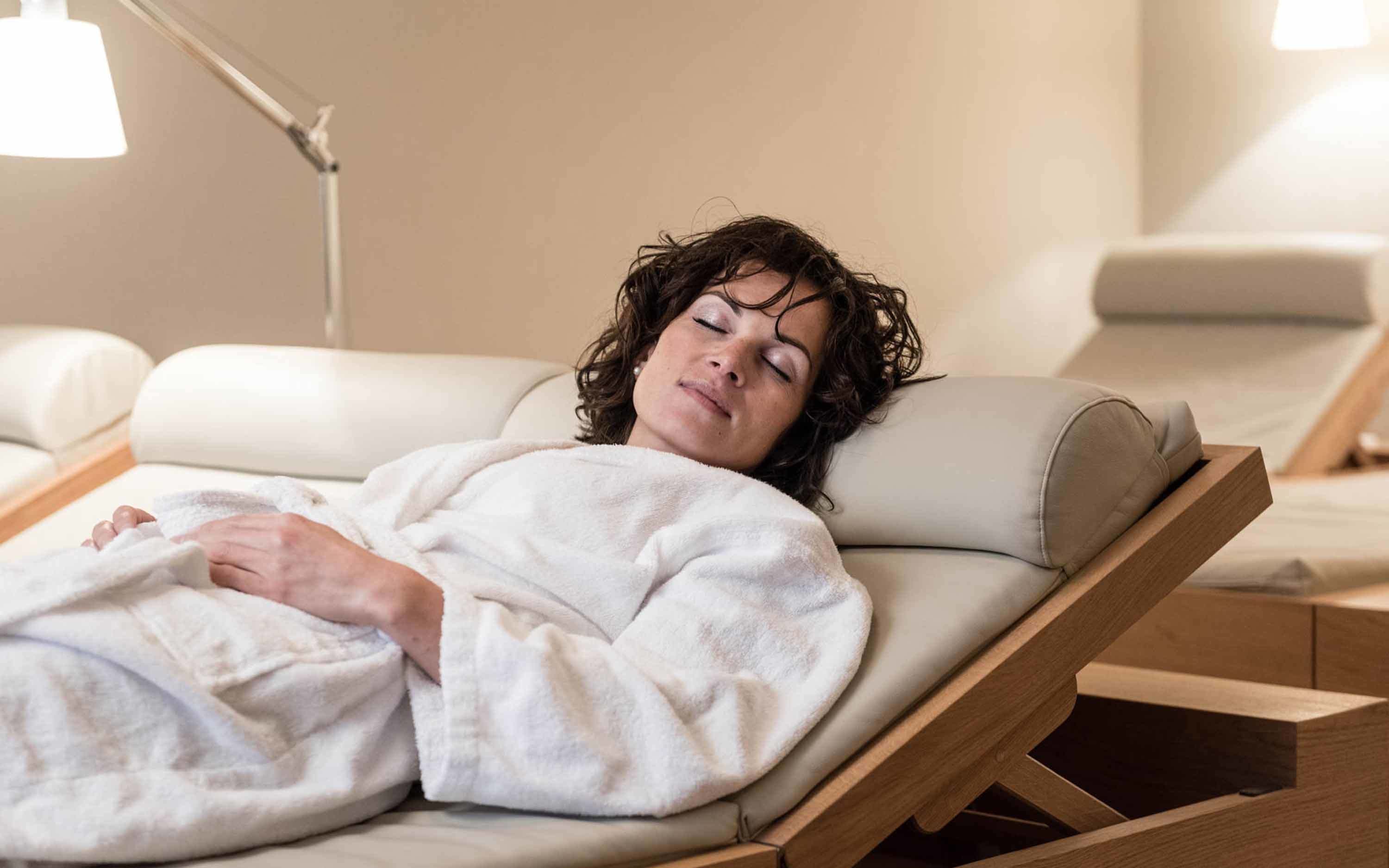 A person lying in a reclining chair in a well-lit room with a lamp in the background.
