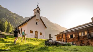 Una iglesia con un campanario, un edificio de madera y excursionistas en una colina cubierta de hierba.
