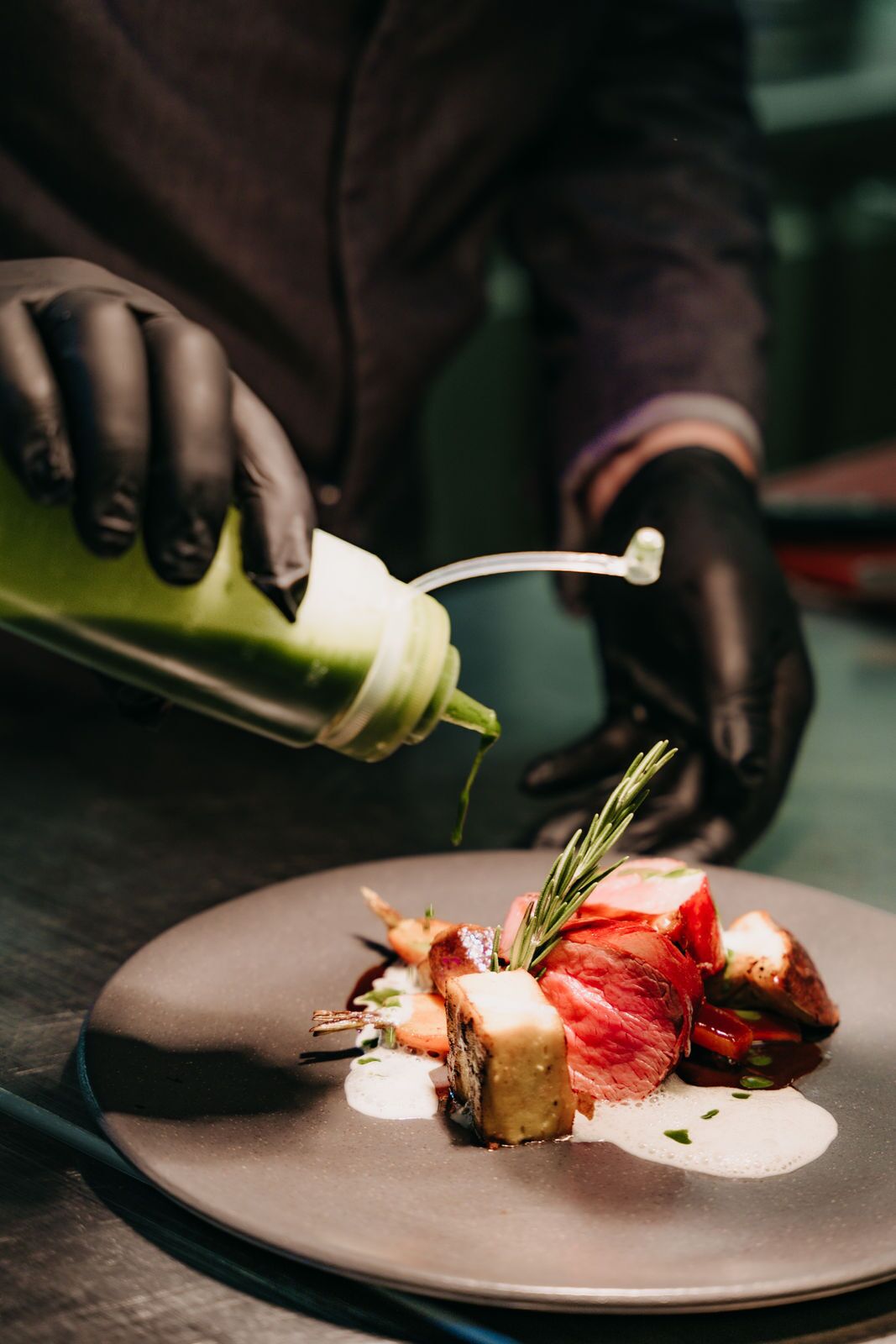 A chef pouring a green sauce onto a plate with food.