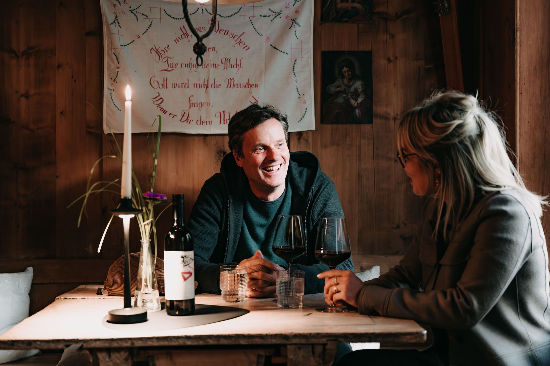 A wooden interior with a table set for two, featuring a candle, wine bottle, and glasses.