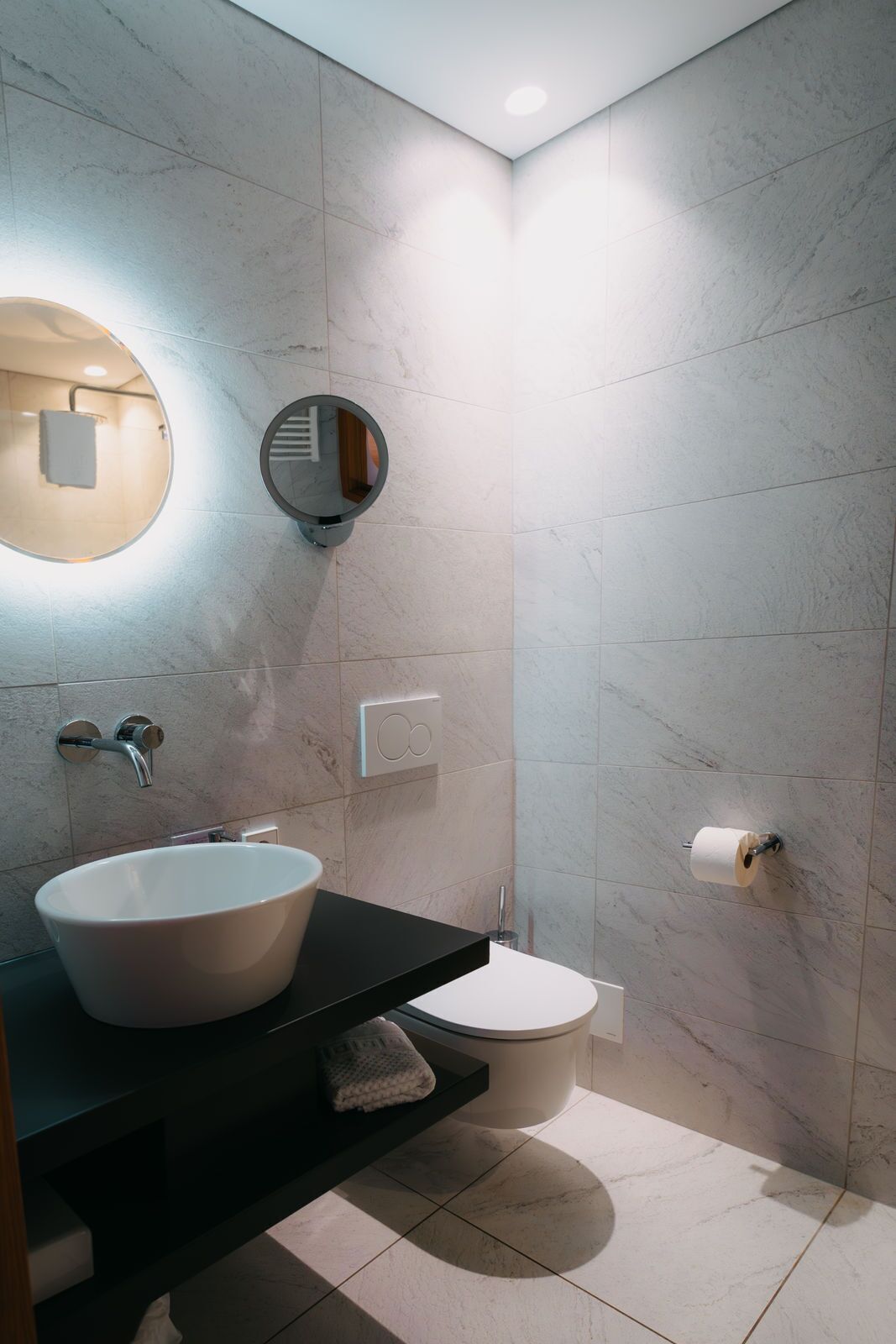 A modern bathroom with a round mirror, a sink, a toilet, and a towel rack.