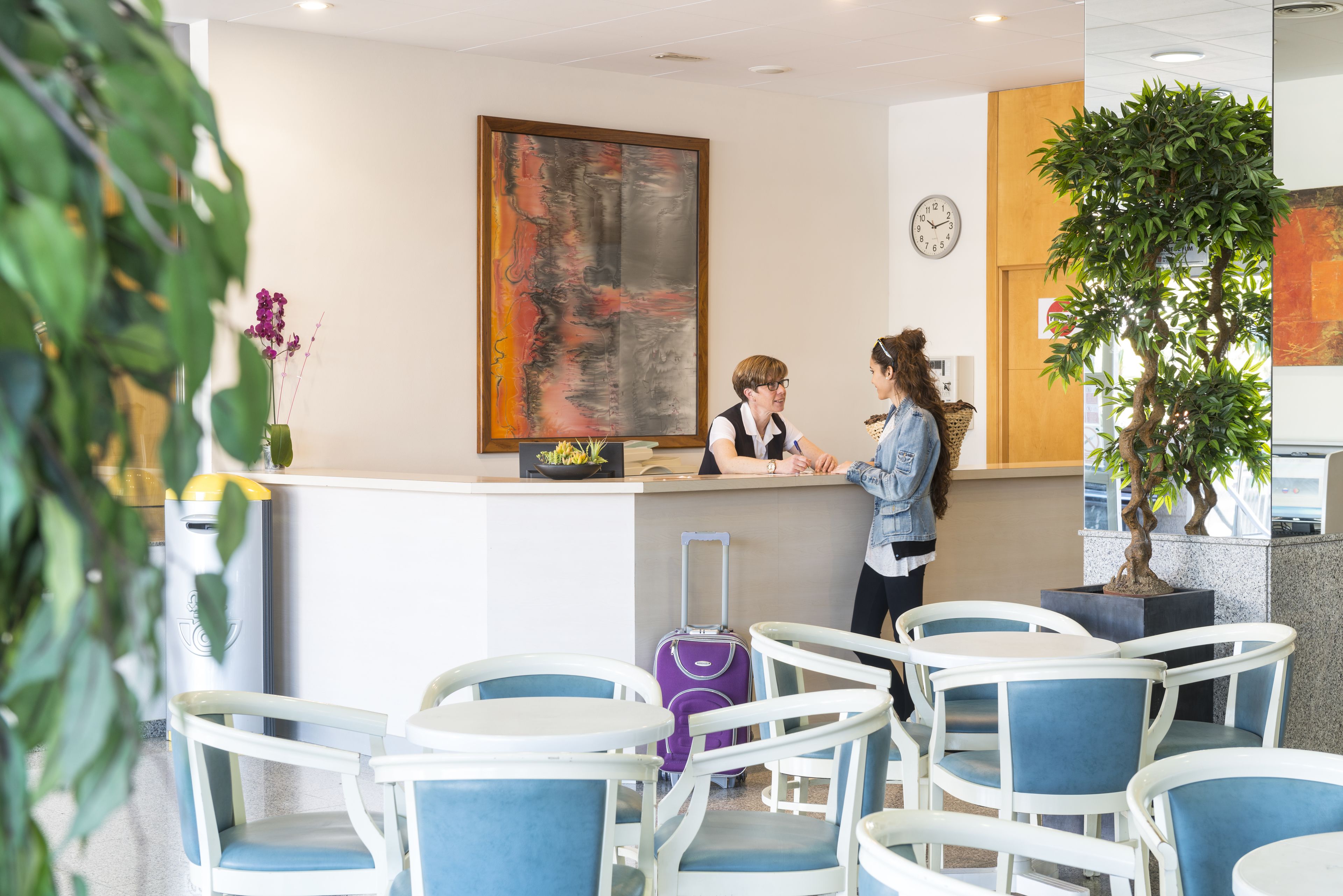 A reception area with a counter, chairs, a clock, and a large abstract painting.