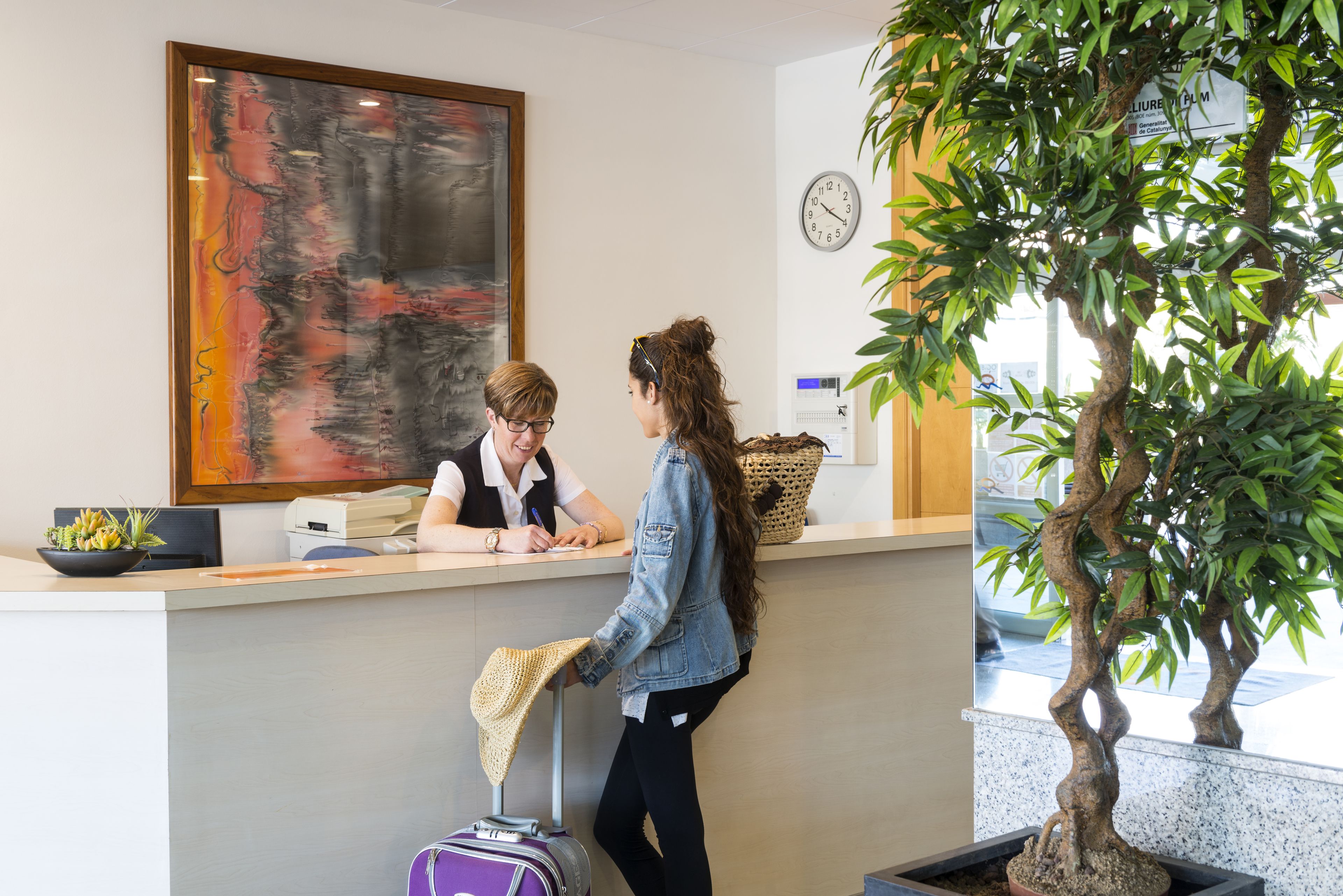 Een receptiebalie met een groot abstract schilderij, een klok en een potplant.